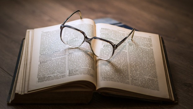 Bild på en uppslagen bok och ett par glasögon som ligger ovanpå.