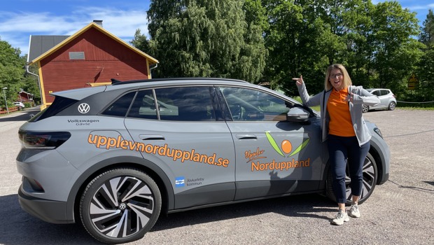 Bild på näringslivsutvecklare Linda Helzenius tillsammans med bilen som är märkt med Upplev Norduppland samt Älvkarleby kommuns logotyp